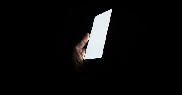 A hand holding a glowing smartphone in a completely dark room