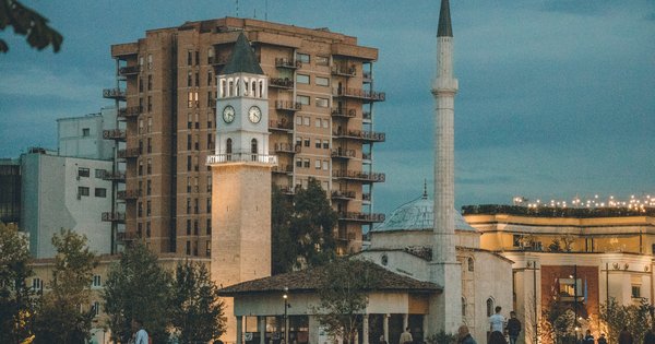 Tirana's lit-up Clock Tower and the minaret of the Et'hem Bey Mosque at dusk, with people strolling across Skanderbeg Square