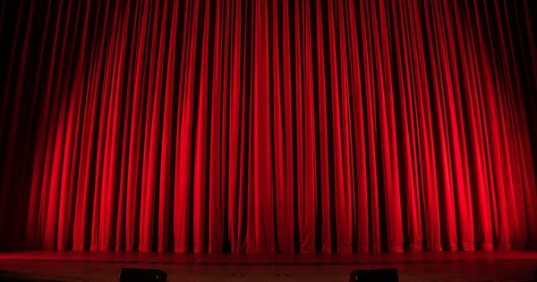 A red velvet theatre curtain lit from below, closed over an empty stage
