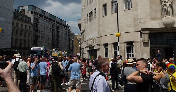 Crowds of people at London Pride 2011 on Portland Place outside BBC Broadcasting House, a pale stone building with a carved statue above the entrance