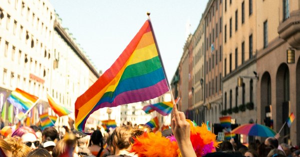 A crowd holding rainbow flags gathers in a European city square ahead of a Pride march