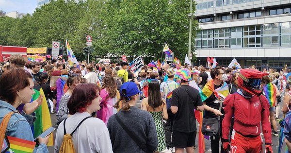 A crowd with rainbow, trans and progress Pride flags fills a Berlin street at Christopher Street Day 2022, with a hand-lettered sign reading “Protect Trans Youth”
