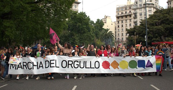 Marchers hold a large 'Marcha del Orgullo' banner at the head of the Buenos Aires Pride march, with rainbow flags and apartment buildings behind them