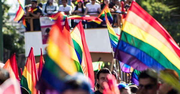 A crowd holding rainbow Pride flags aloft at a Pride march