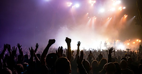 A crowd with raised hands silhouetted against a stage washed in purple and blue light