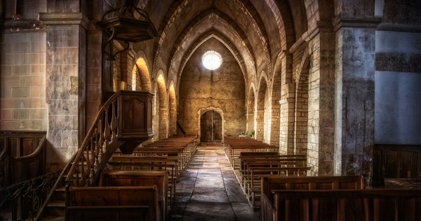 A church interior with wooden pews and light streaming through tall windows