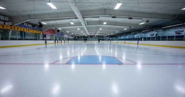 An empty indoor ice hockey rink under bright lights, with a freshly cleaned ice surface and blue centre markings