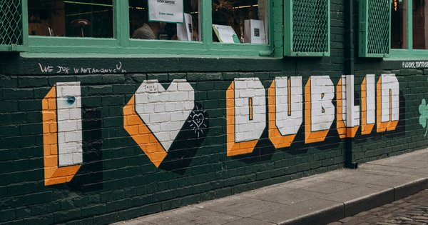 An 'I love Dublin' mural painted in orange, white and green on a dark green brick wall beside a cobbled street