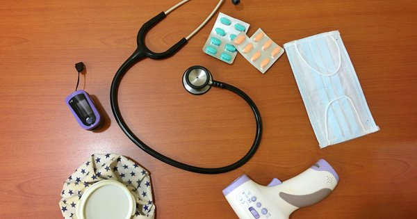 A stethoscope, blister packs of pills and other medical supplies on a wooden table