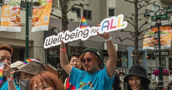 Marchers at Tokyo Rainbow Pride 2024 in Shibuya, one holding up a sign that reads Well-being for ALL next to a small rainbow flag