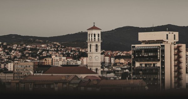 Pristina's skyline at dusk, with the bell tower of the Cathedral of Saint Mother Teresa rising above rooftops and green hills behind