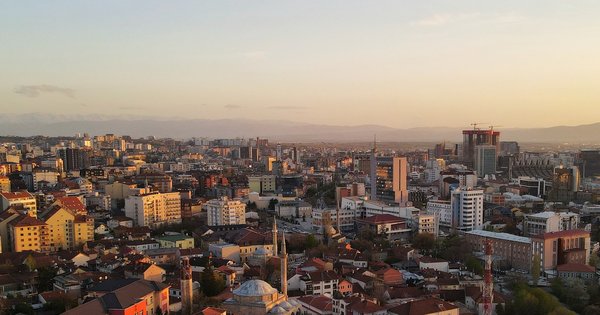 Aerial view of Pristina, Kosovo, at sunset, with apartment blocks, a mosque dome and mountains on the horizon