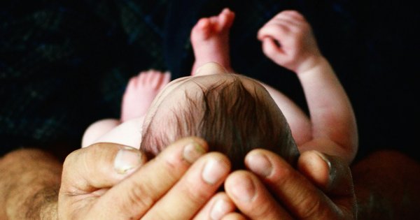 An adult's hand gently holding a newborn baby's tiny hand
