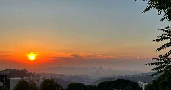 An orange sun setting over the hazy skyline of Beirut, seen from the hills above the city