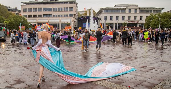 A marcher seen from behind trails a long pink, white and blue trans flag train across a wet square in Podgorica during Montenegro Pride Week 2023