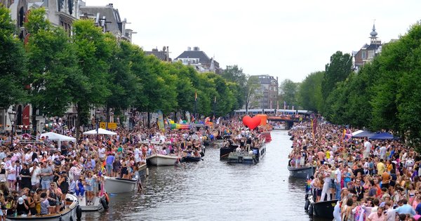 Boats decorated with rainbow flags sailing along an Amsterdam canal during Pride