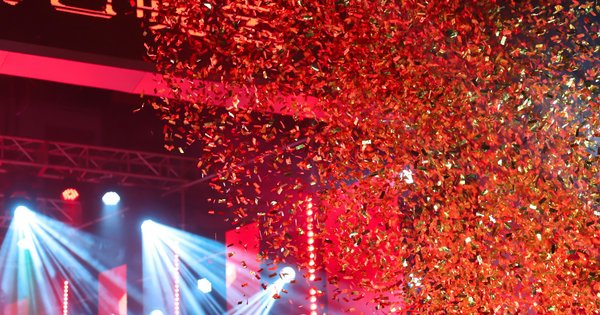 Red and gold confetti pouring down over a concert stage lit by blue spotlights