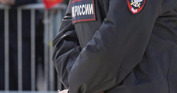 A Russian police officer in a dark jacket with an 'МВД России' shoulder patch, standing by metal crowd barriers