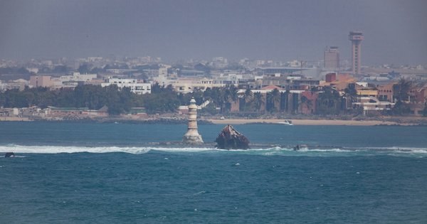 The Dakar shoreline seen across the Atlantic, with a small white lighthouse in the water and the city skyline behind it