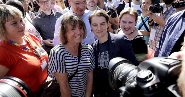Ana Brnabić, in a dark blazer and T-shirt, smiles with marchers surrounded by press cameras at the Belgrade Pride march in September 2017