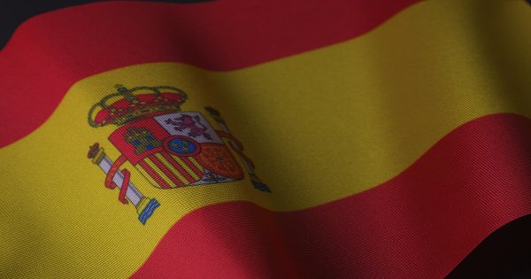 The flag of Spain waving in the wind against a blue sky