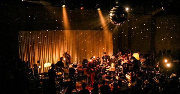 A mirror ball hanging above a dimly lit stage, lit by warm spotlights in front of a gold curtain