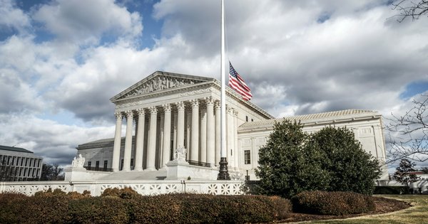 The U.S. Supreme Court building in Washington, D.C., under a cloudy sky, with the American flag flying
