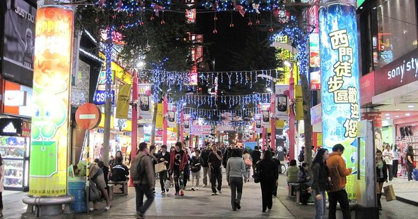 A busy pedestrian street in Taipei's Ximending district at night, lit by neon shop signs