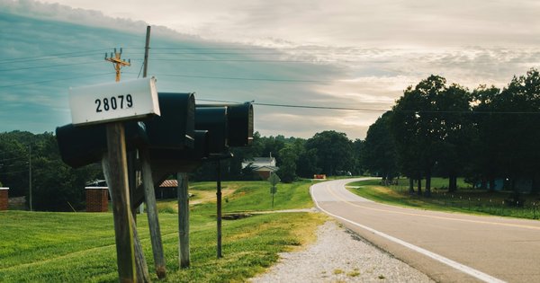 A row of black rural mailboxes on wooden posts beside a winding country road under a cloudy sky