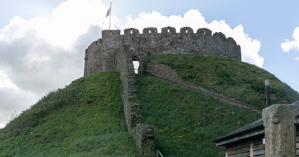 The round stone keep of Totnes Castle on top of its grassy motte in Devon, under a blue sky with white clouds