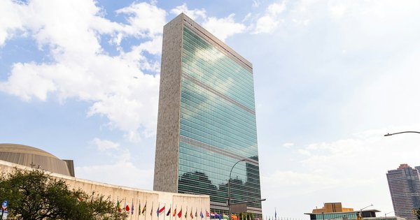 The glass Secretariat tower of United Nations headquarters in New York, with member-state flags along the plaza