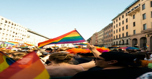 Crowds of marchers with rainbow flags moving through an Amsterdam street during a pride parade