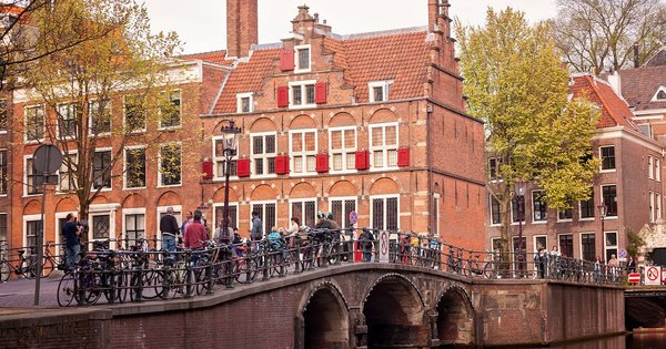 Crowds and rainbow flags along an Amsterdam canal during Pride.
